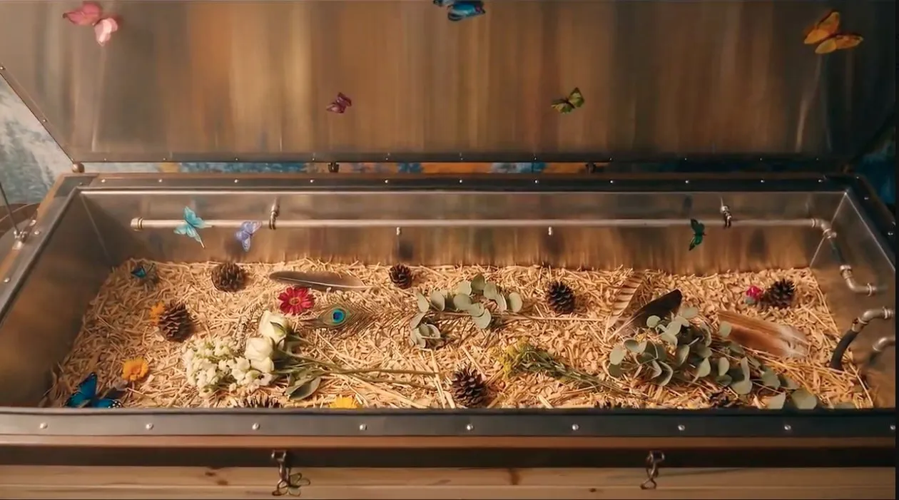 An open terramation vessel bedded with straw and wood chips, scattered with flowers, feathers, and pine cones